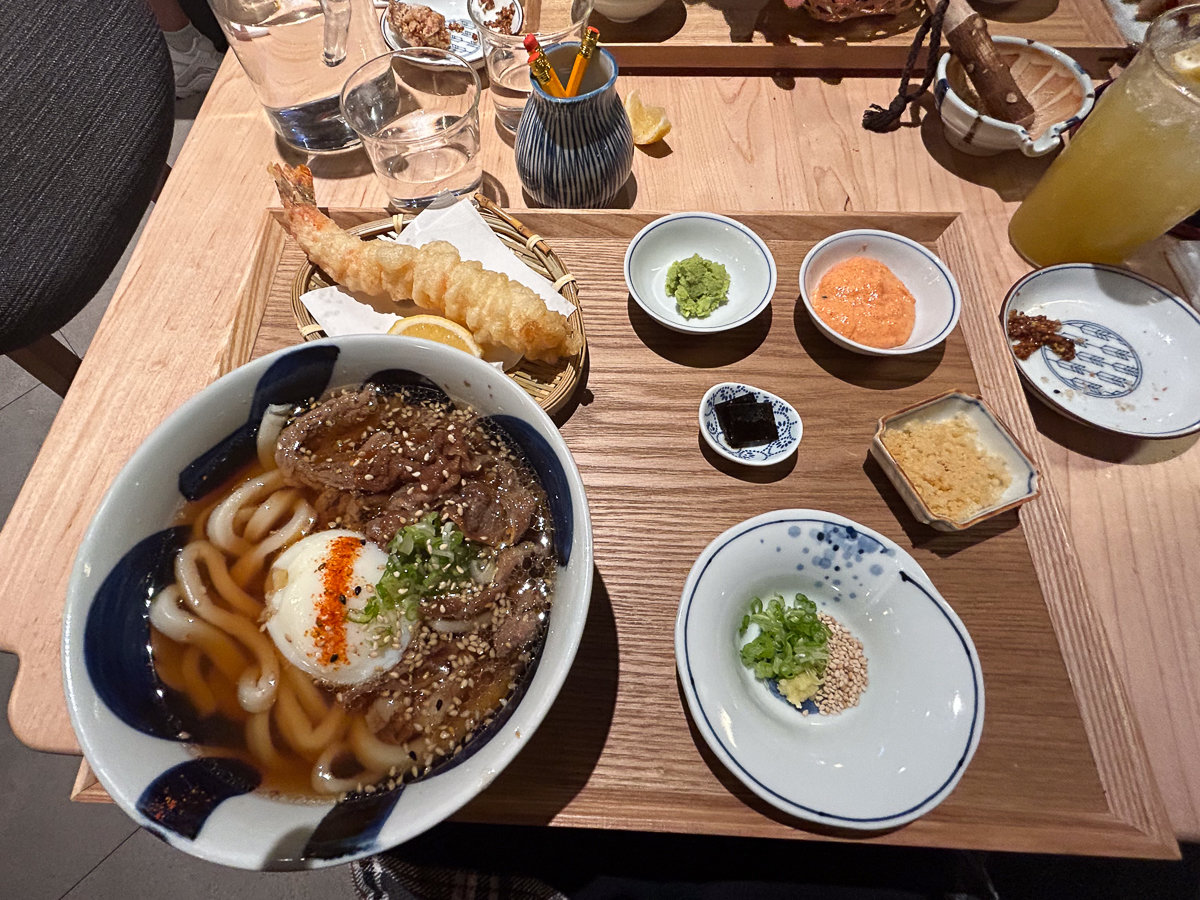 udon bowl with meat and small dishes with toppings